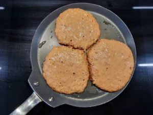 Drei Pancakes mit gebräunter Oberfläche in einer Pfanne.