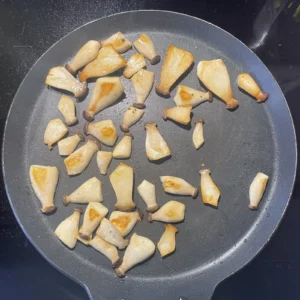 Kräuterseitlinge mit goldbraunen Schnittflächen in der Pfanne.